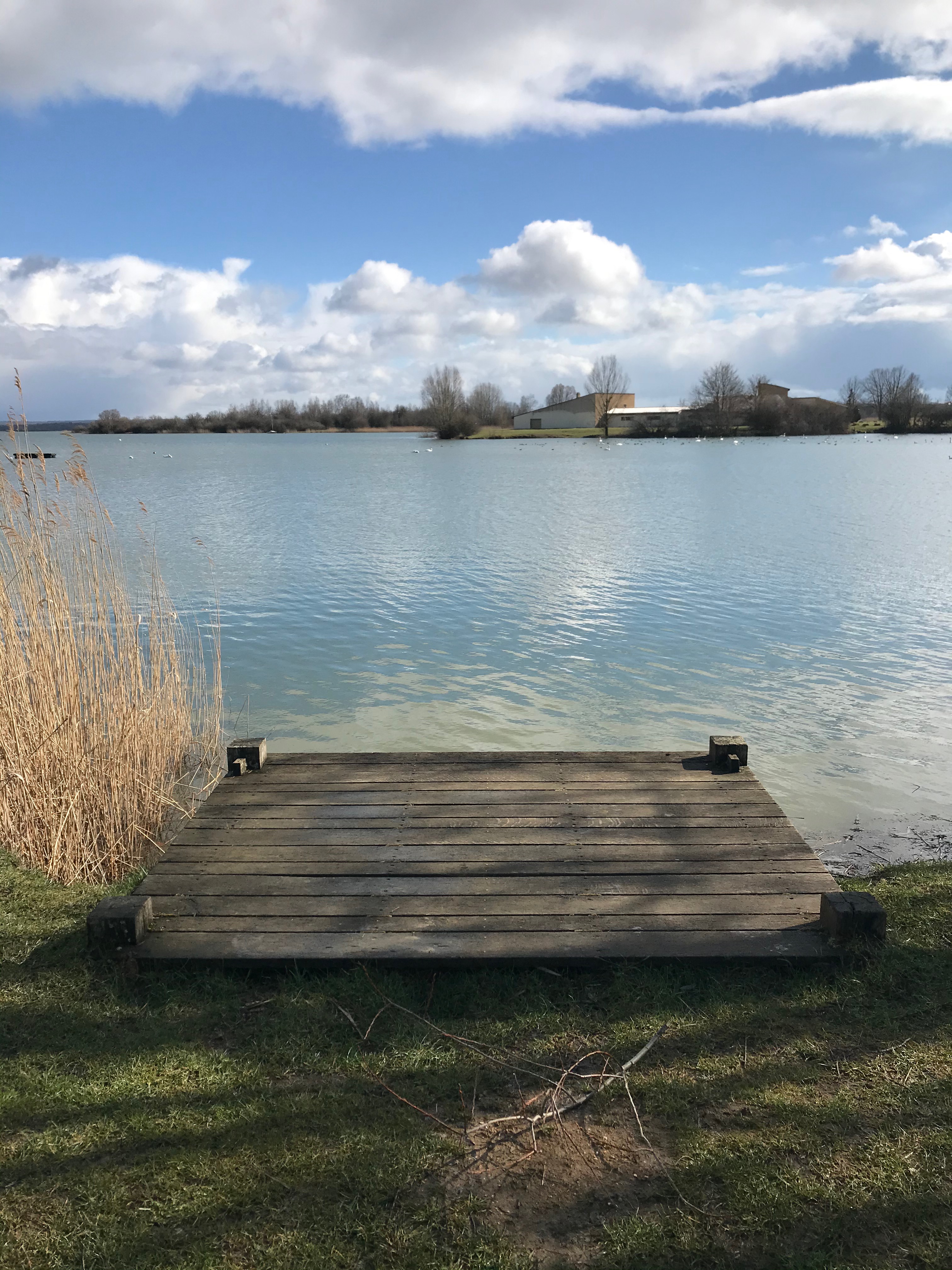 un ponton en bois qui donne sur le lac, l'eau est bleu clair, le ciel bleu se reflète dans le lac.