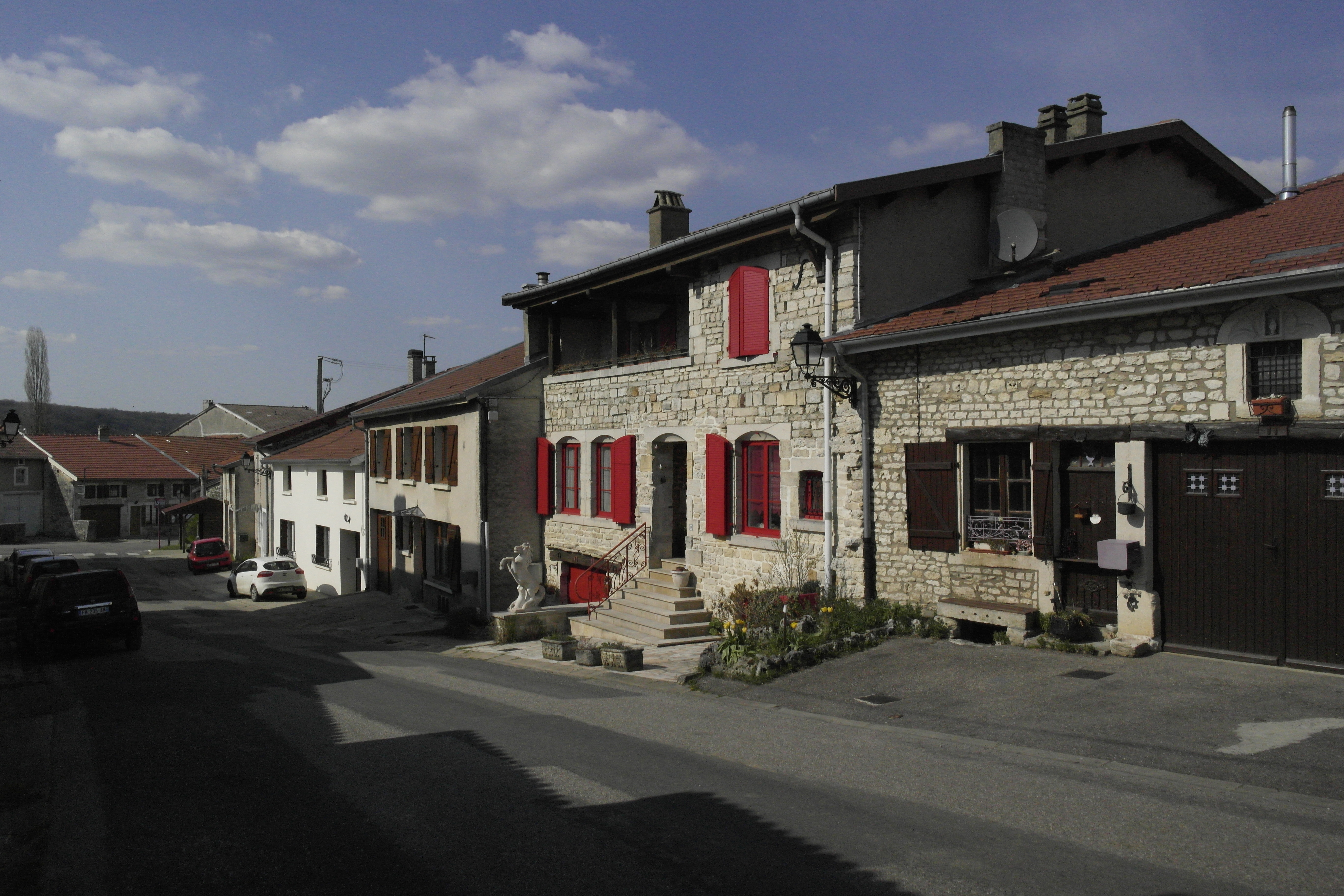 Vue d'une rue de Longeaux, en premier plan deux maisons en petites pierres maçonnées, dont une avec des volets rouges.