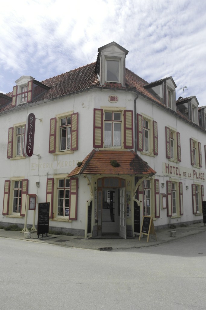 devanture d'un hôtel blanc avec des volets beige et rouge, fait l'angle de deux rues