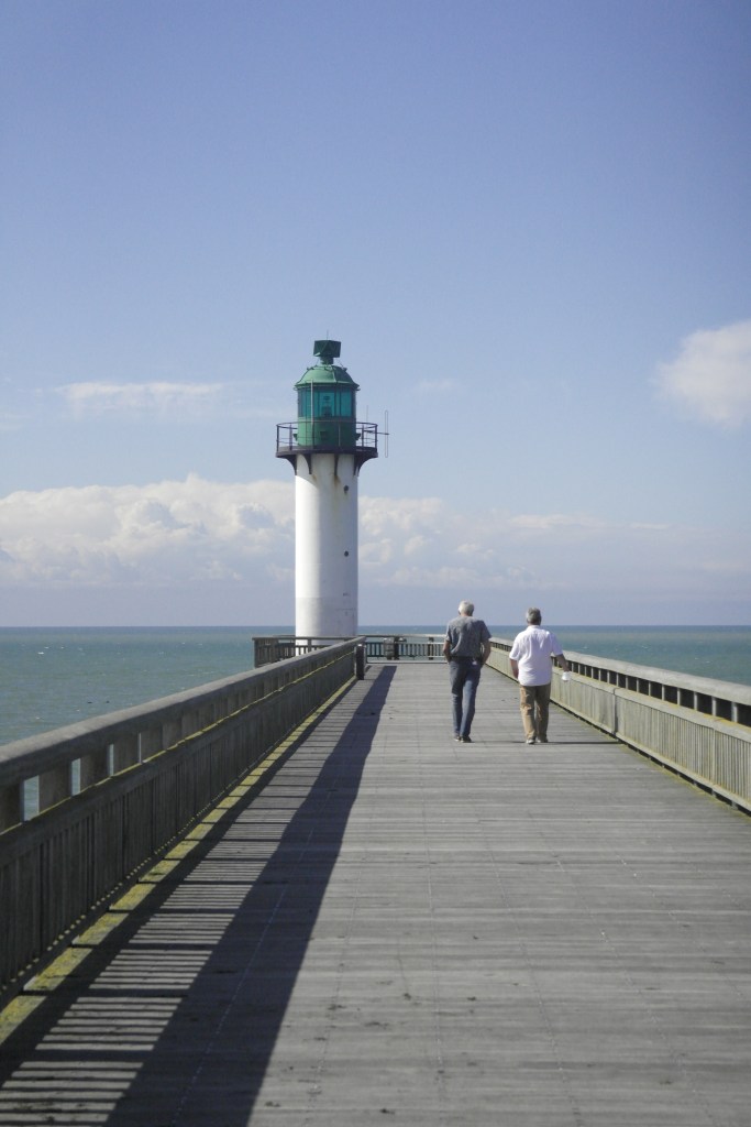 jetée en bois avec un phare au bout, blanc et vert, deux hommes marchent devant