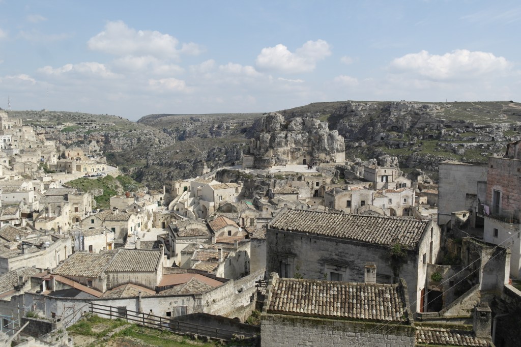 Vue d'un quartier de Matera et nature environnante, au milieu au second plan l'église Santa Maria de Idris, taillée dans un rocher.