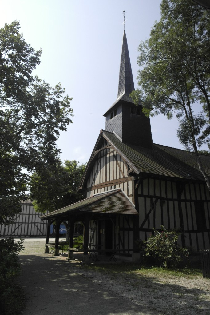 église de Champagne avec ses colombages et un clocher fin noir