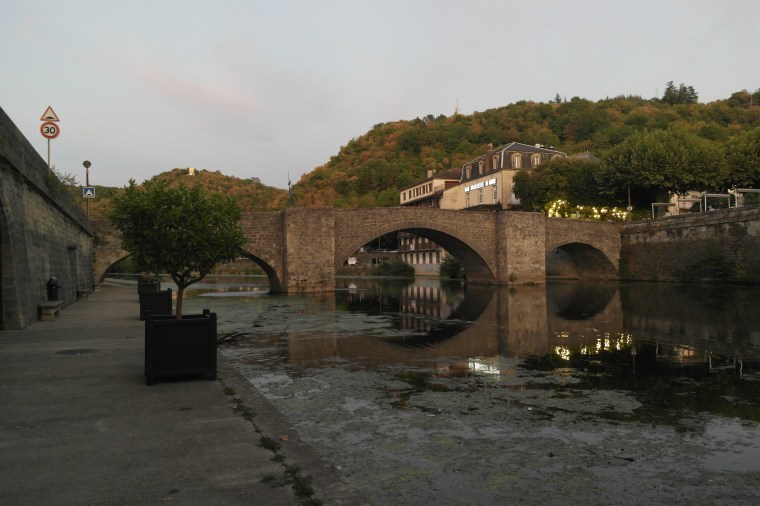 pont de pierre au-dessus d'une rivière et berge aménagée avec des arbustes en pot