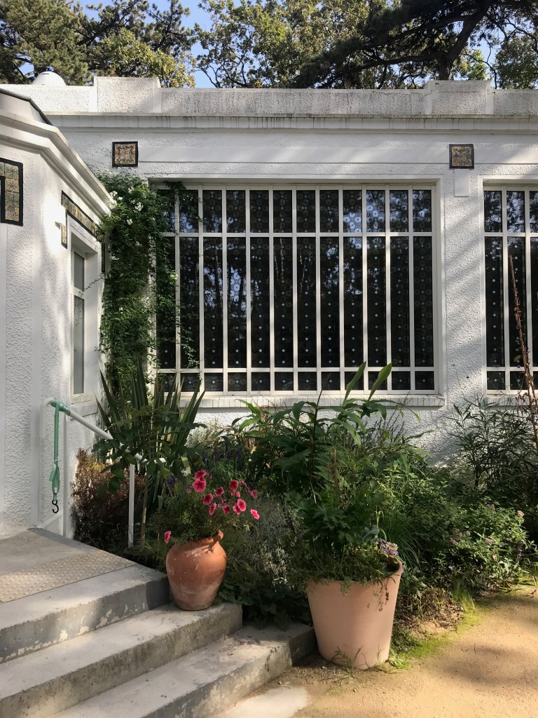 entrée d'un bâtiment blanc aux grandes fenêtres, plantes en pot devant