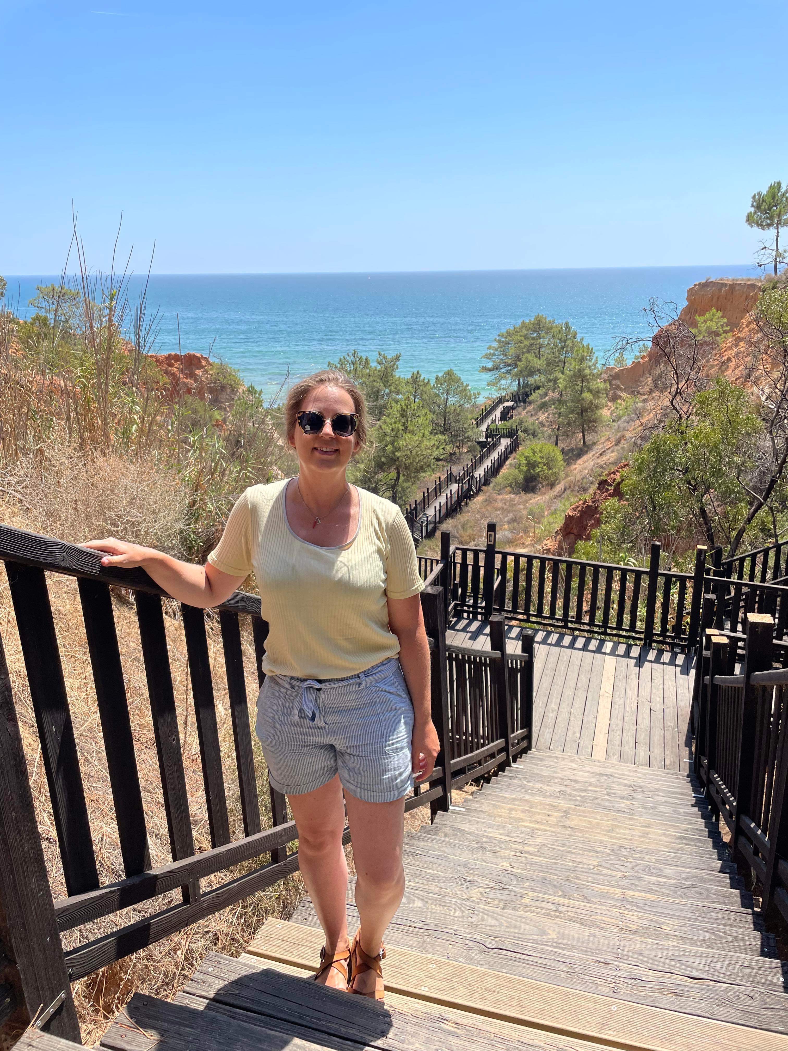 femme debout sur des escaliers, paysage de pinède et mer cristalline